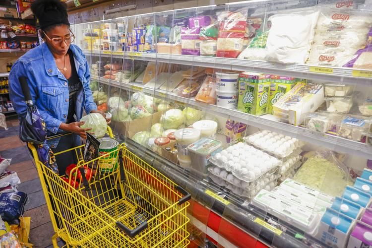 A woman loads a cabbage into a yellow grocery cart while passing by a refrigerator section in a supermarket.